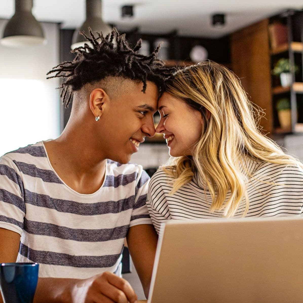 Zwei junge Leute sitzen vor einem Laptop und stecken die Köpfe zusammen.